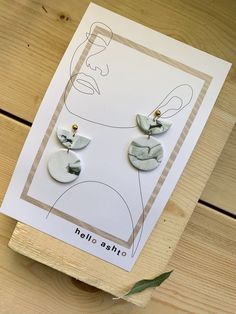 a pair of earrings sitting on top of a piece of paper next to a card