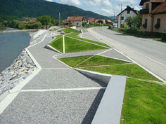 an empty street next to a river with houses on the other side and mountains in the background