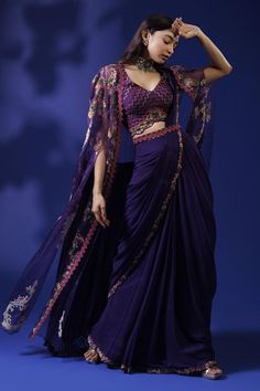 Purple pre-draped saree with multicolor thread embroidered border in floral pattern. Paired with chevron embroidered blouse, cape and belt.
Components: 4
Pattern: Embroidery
Type Of Work: Thread
Neckline: Blouse: V neck, Cape: Open
Sleeve Type: Blouse: Sleeveless, Cape: Flared sleeves
Fabric: Raw Silk, Georgette, Organza
Color: Purple
Other Details: 
Scallop bordered blouse
Occasion: Sangeet - Aza Fashions Designer Blouse Piece With Resham Embroidery And Cape Sleeves, Designer Cape Sleeves Blouse Piece With Resham Embroidery, Reception Blouse Piece With Cape Sleeves And Dupatta, Blouse Piece With Cape Sleeves And Dupatta For Reception, Silk Saree With Cape Sleeves For Reception, Designer Saree With Zari Work And Cape Sleeves, Reception Blouse Piece With Dupatta And Cape Sleeves, Anarkali Pre-draped Saree With Sheer Dupatta And Cape Sleeves, Bollywood Saree With Cape Sleeves And Dupatta