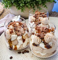 two glasses filled with desserts sitting on top of a table next to a potted plant