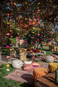 an outdoor seating area with colorful pillows and flowers on the grass, in front of a tree