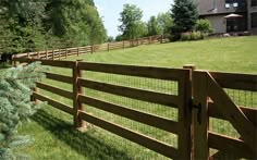 a wooden fence in the middle of a grassy field next to a large house and trees