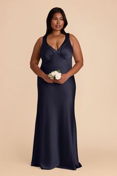 a woman in a dark blue dress holding a white flower and posing for the camera