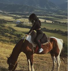 a woman riding on the back of a brown and white horse in an open field