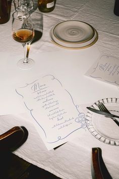 the table is set with wine glasses, plates and menus for an elegant dinner