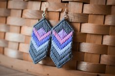 a pair of earrings hanging from a wooden wall next to a woven piece of wood