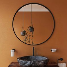 a round mirror hangs above a sink in a bathroom with an orange wall and wooden countertop