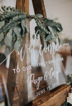 a welcome sign with greenery is displayed on a wooden easel in front of a window