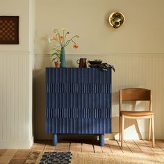 a blue cabinet sitting in the corner of a room next to a chair and vase with flowers