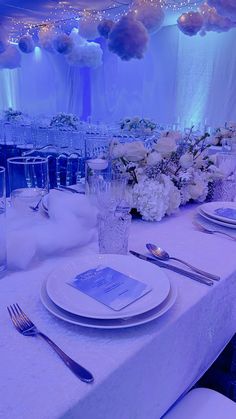 the table is set with white flowers and silverware for an elegant wedding reception in blue lighting