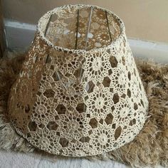 a crocheted lamp shade sitting on top of a furry rug next to a wall