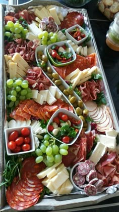 an assortment of meats and cheeses on a platter with grapes, tomatoes, olives, bread