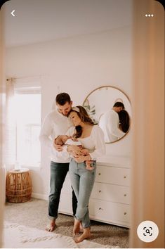 a man and woman standing in front of a mirror holding their newborn son, who is looking at his belly