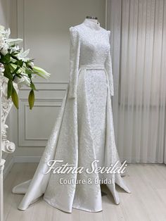 a white wedding dress on display in front of a vase with flowers and greenery