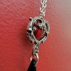 A delicate pewter heart pendant by Alchemy Gothic, the center piece enameled in a transparent red and surrounded by an antiqued pewter Baroque frame with a skull profile on either side. There is a black crystal teardrop suspended below and the pendant hangs from a pewter bale. Pendant Width 0.87" x Height 1.89" x Depth 0.31" and Weight: 0.35 ozChain Length approx. measuring 32" total. Pendant hangs from a nickel-free chain with clasp fastener. Trace chain. Fine English Antiqued Pewter Gothic Heart Pendant Jewelry, Gothic Heart Pendant Metal Jewelry, Gothic Metal Jewelry With Heart Charm, Gothic Necklace With Heart Charm, Gothic Teardrop Silver Jewelry, Gothic Silver Teardrop Jewelry, Red Gothic Heart Pendant Jewelry, Gothic Silver Jewelry With Heart Charm, Silver Gothic Jewelry With Heart Charm