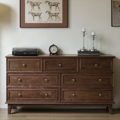 a wooden dresser sitting next to a wall with pictures above it and a clock on top