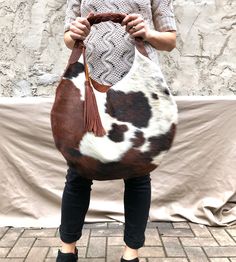 "Add lining to any of our bags https://www.etsy.com/listing/891051352 Unique cowhide leather hobo bag, with brown braided strap and two tassels (included) Measurements- 19\" wide x 19\" high 14\" high in the middle This is a large size, slouchy, handmade leather bag, with feminine design and a braided black strap. Made with soft hair on leather leather. The bag is great for your daily essentials, perfect for everyday use, or for a special occasion. It can hold your school items, groceries, walle Cowhide Bags Handbags, Hair On Leather Bags, Cow Print Bag, Leather Hobo Bags, Cowhide Purse, Leather Hip Bag, Unique Handbags, Cowhide Bag, Stylish Purse