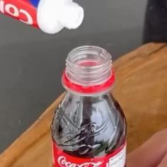 a person holding a toothbrush over a coca - cola bottle on top of a wooden table