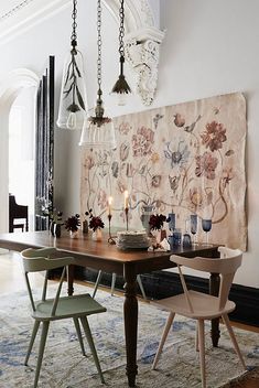 a dining room table with chairs and a large tapestry hanging on the wall behind it