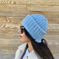 a woman wearing a blue knitted beanie hat standing in front of a wooden wall