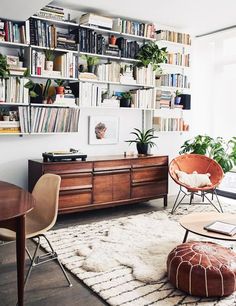 a living room filled with furniture and bookshelves next to a large window covered in plants