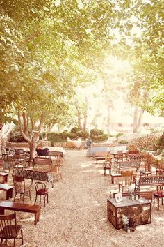 there are many tables and chairs in the park with lots of trees on each side