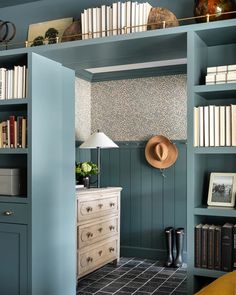 a room with bookshelves and a dresser in the corner that has a hat on top of it