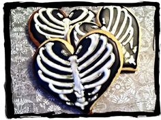 two heart shaped cookies decorated with white icing and black frosting on a table