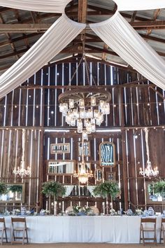 the inside of a barn with tables and chairs set up for a wedding reception in front of a chandelier