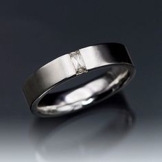 a white gold wedding ring with a diamond set in the center, on a reflective surface