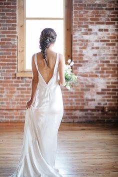 a woman in a white dress is holding a bouquet and looking out the window at something