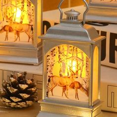 three lit up deer lanterns sitting on top of a wooden table next to pine cones