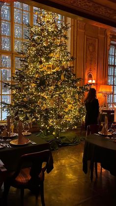 a large christmas tree is lit up in the middle of a room with tables and chairs