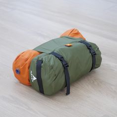 an orange and green duffle bag laying on the floor with it's straps down