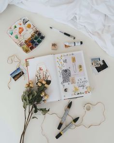 an open notebook surrounded by markers, flowers and other items on a white tablecloth