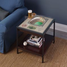 a table with books and a beer on it in front of a blue couch next to a sofa