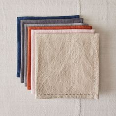 five different colored linen napkins sitting on top of a white surface with stitching