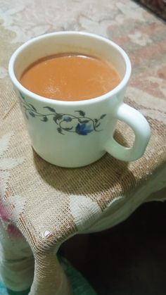 a cup of tea sitting on top of a table next to a cloth covered stool