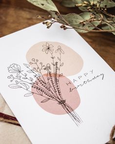 a card with some flowers on it sitting on top of a piece of paper next to a plant