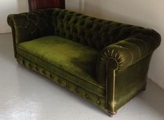 a green velvet couch sitting on top of a white floor next to a wooden door