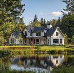 a large white house sitting next to a lake in the middle of a lush green forest