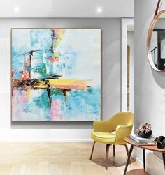 an abstract painting hangs on the wall above a yellow chair and table in a white room