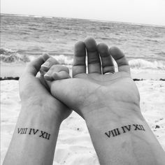 two people are holding hands with roman numerals on their wrists and the ocean in the background