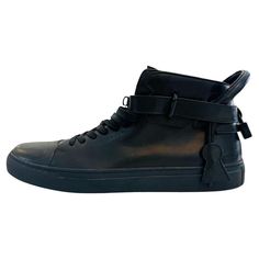 Buscemi Leather High-Top Sneakers With Padlock Detail Black lace-up sneakers designed with round toe and strap around the ankle. Detailed with black 'Buscemi' engraved padlock to rear and leather clochette to the side and featuring logo embossment to the tongue. Size – 46 Condition – Very Good Composition – Leather Comes with – Shoes Only Good Composition, Leather High Tops, Designer Sneakers, Shoes Black, High Top, Black Lace, Gift Shop, High Top Sneakers, High Tops