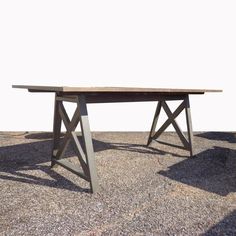 a wooden table sitting on top of a gravel covered ground next to a white wall