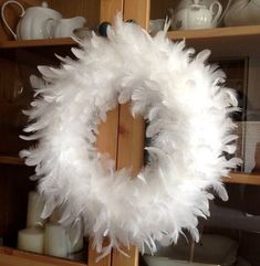 a white feather wreath hanging on a wooden shelf in front of a china hutch