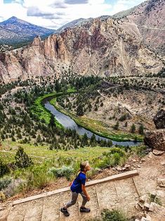 a young boy walking up some steps in front of a valley and mountains with a river running through it