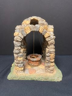 a stone arch with a fire pit in the center on a black surface, next to a gray wall