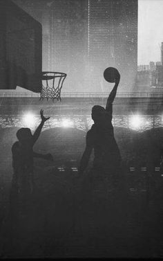 black and white photograph of people playing basketball in the city at night with lights on