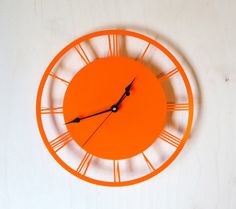 an orange clock with roman numerals is on a white wall and has black hands